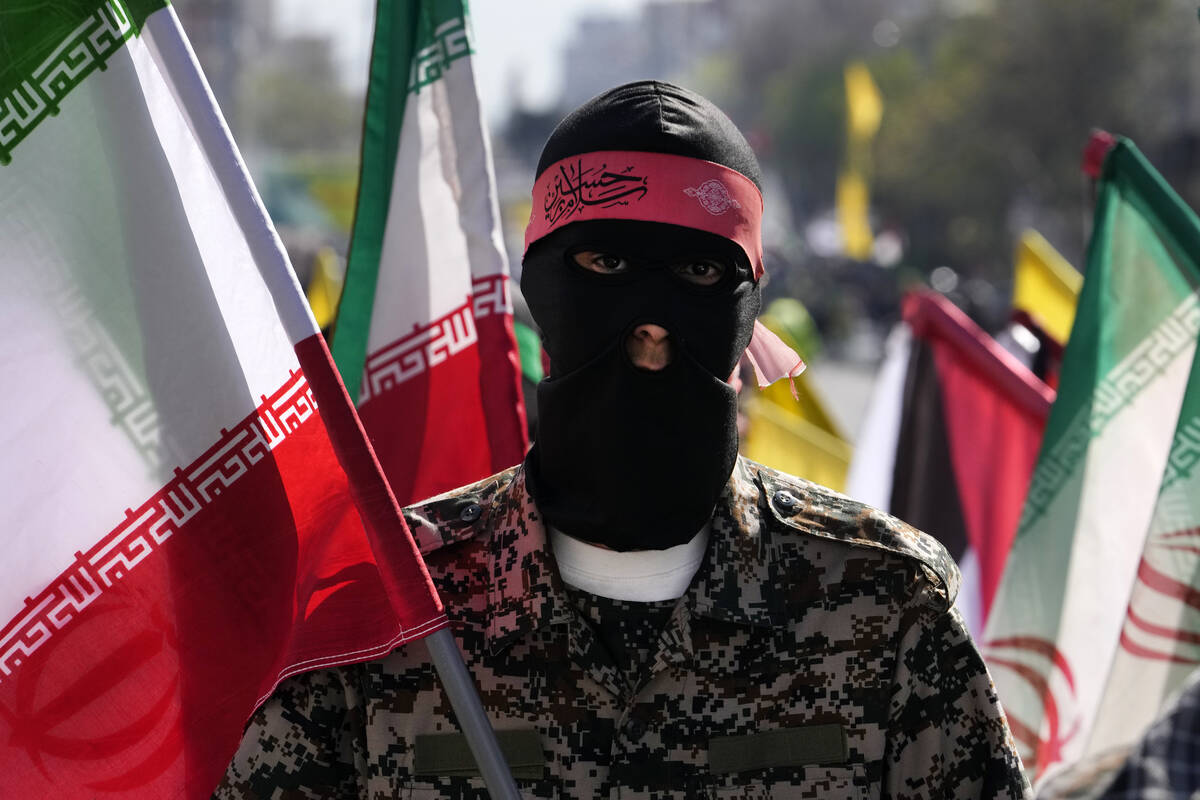 A member of the Iranian paramilitary Basij force holds an Iranian flag as he covers her face in ...