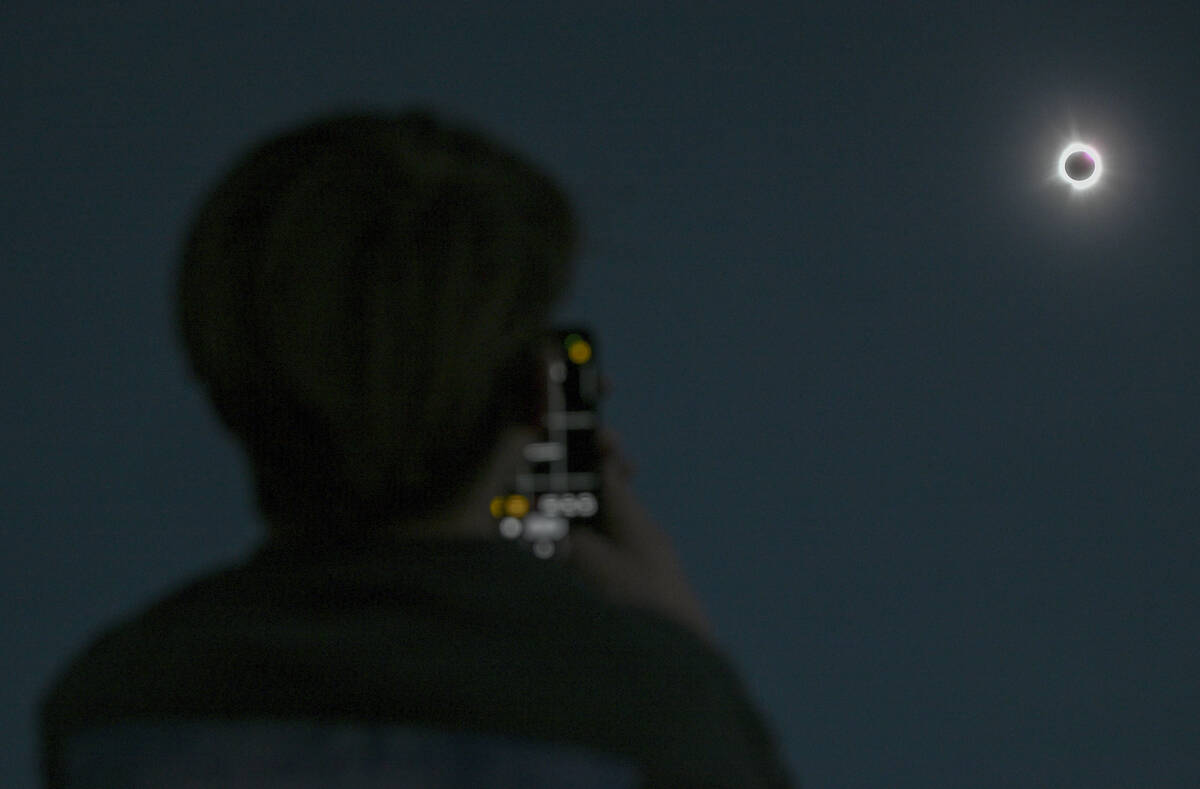 A person takes a photograph of the sun during totality as the moon passes between it and the ea ...