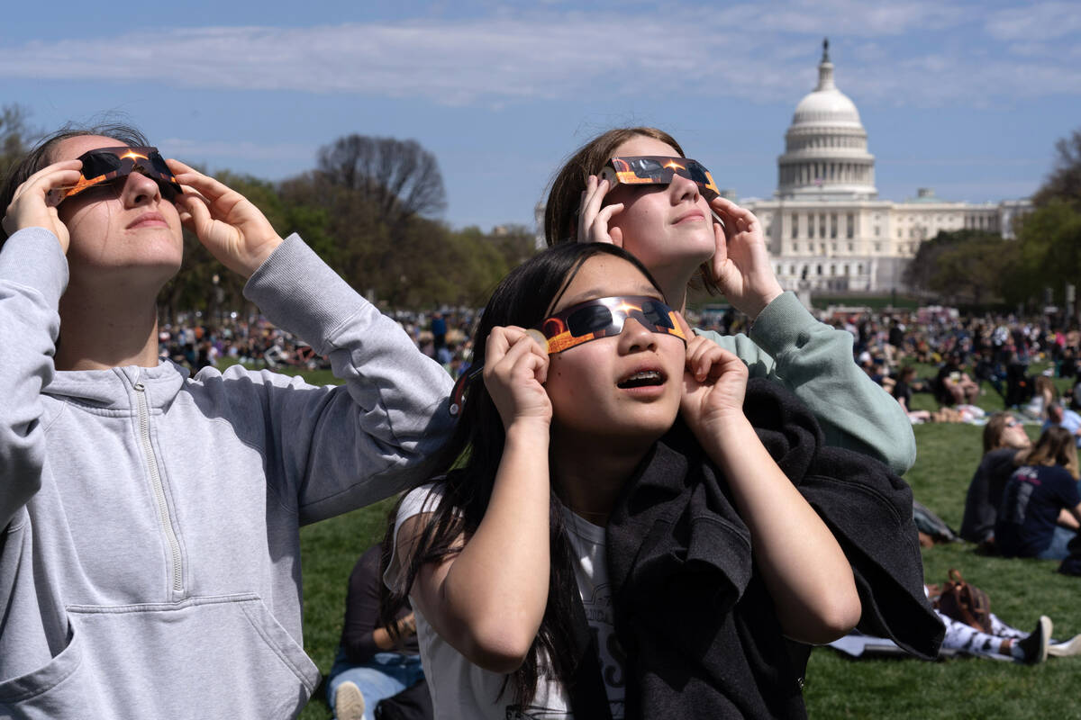 People wear protective glasses as they gather to watch as the moon partially covers the sun dur ...