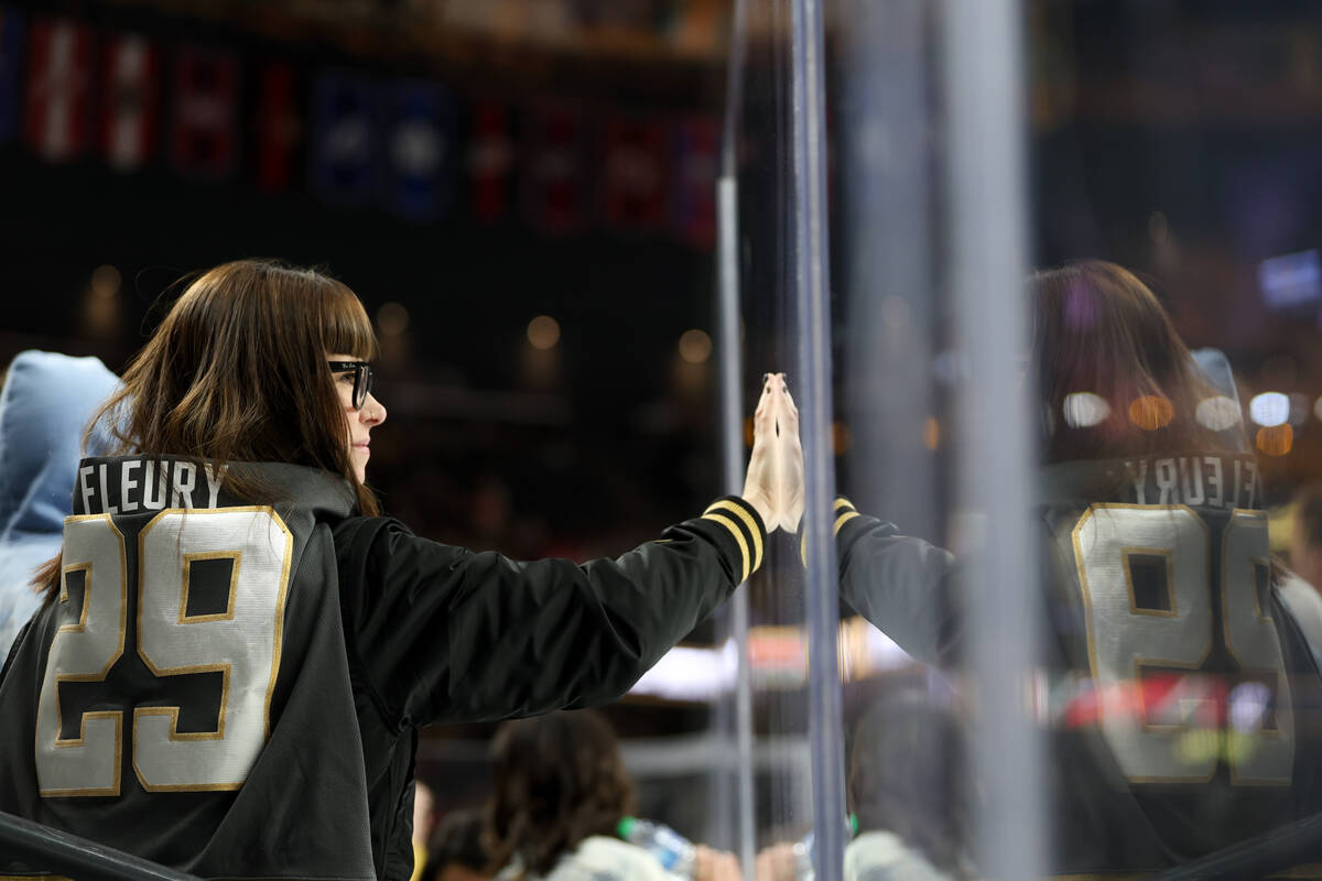 A Golden Knights fan touches the boards while wearing the former Knights jersey of Wild goalten ...
