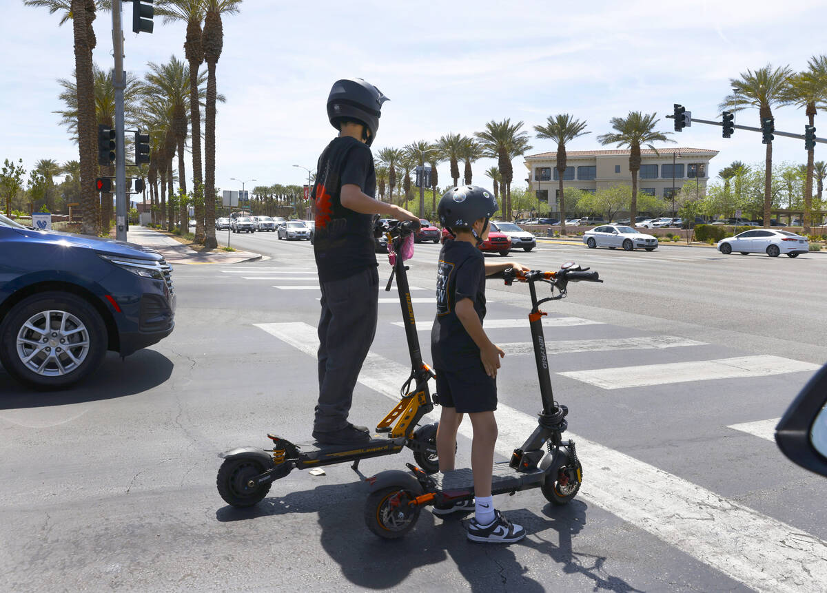 Children on electric scooters wait at a red light on Village Walk Drive near Green Valley Parkw ...