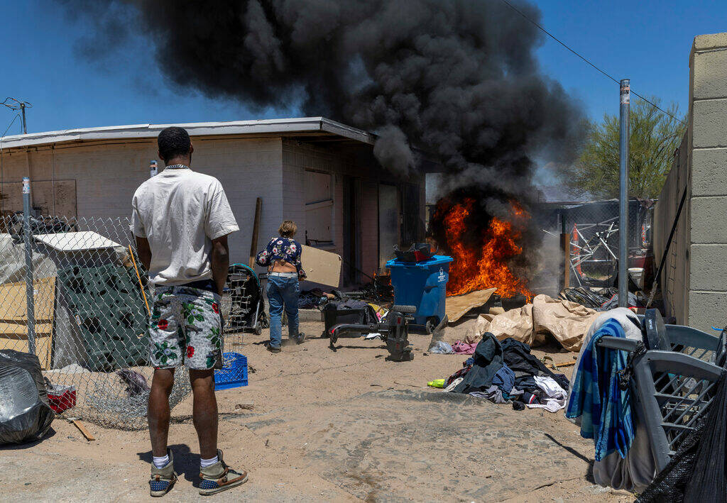 A man watches as a woman attempts to stop a fire from spreading during a house fire between W. ...