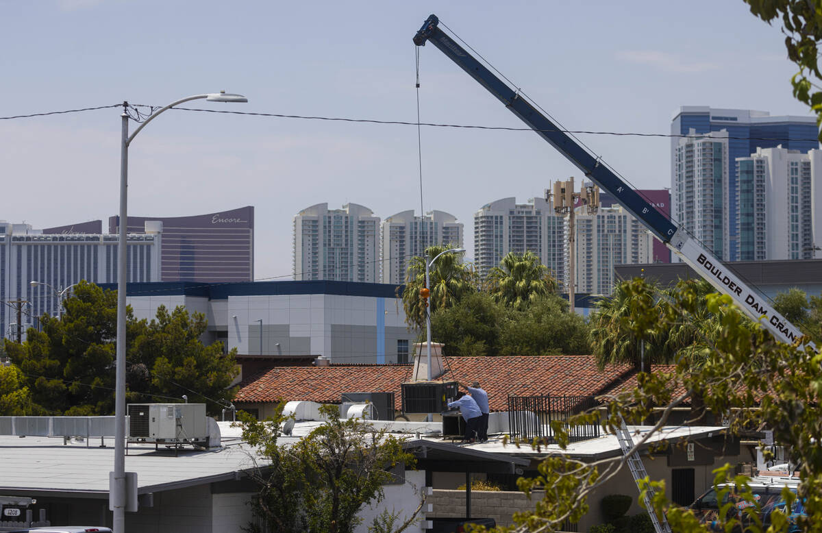 Workers replace an air conditioning unit on the roof of a building at the corner of Maryland Pa ...