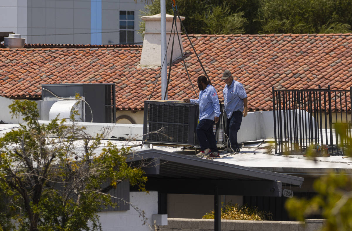 Workers replace an air conditioning unit on the roof of a building at the corner of Maryland Pa ...