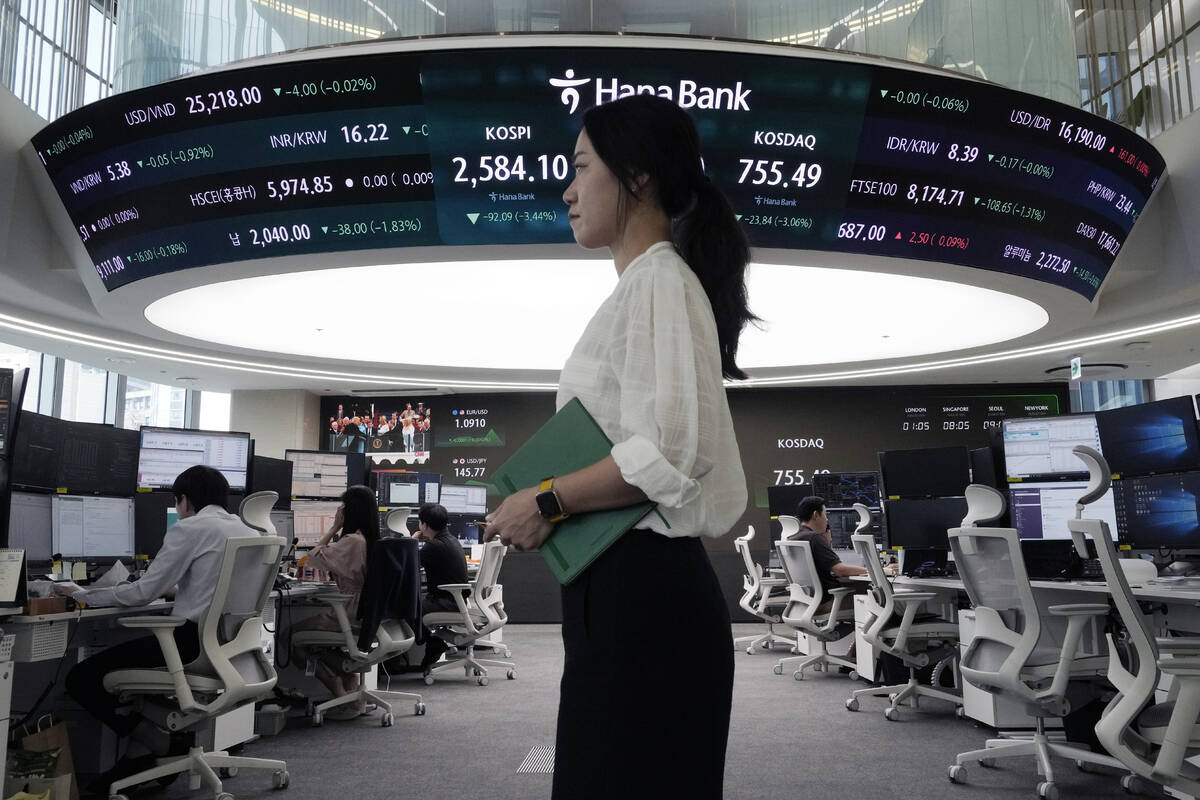 A currency trader passes by a screen showing the Korea Composite Stock Price Index (KOSPI), top ...