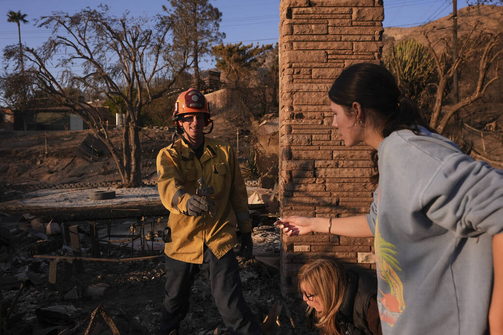 Glendale Fire Department captain Chris Jernegan, left, holds a cross he found as he helps Ella ...