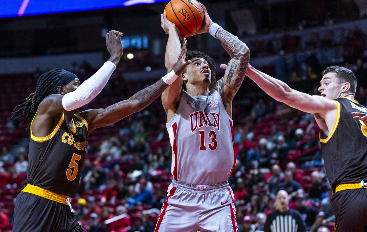 UNLV guard Brooklyn Hicks (13) splits the defense of Wyoming Cowboys guard Obi Agbim (5) and fo ...
