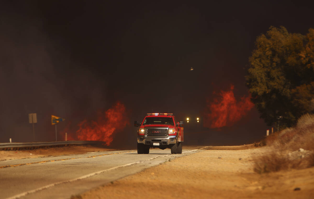 A fire truck drives past flames caused by the Hughes Fire in Castaic, Calf., Wednesday, Jan. 22 ...