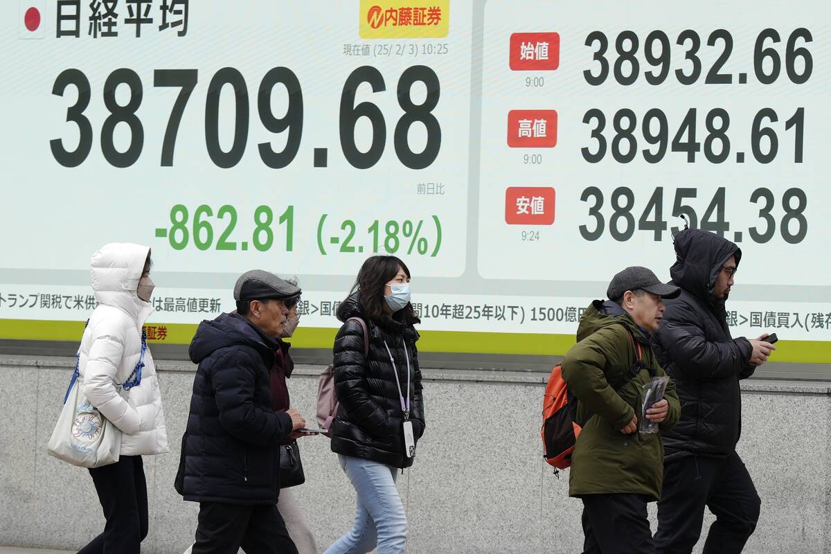 People walk in front of an electronic stock board showing Japan's Nikkei index at a securities ...