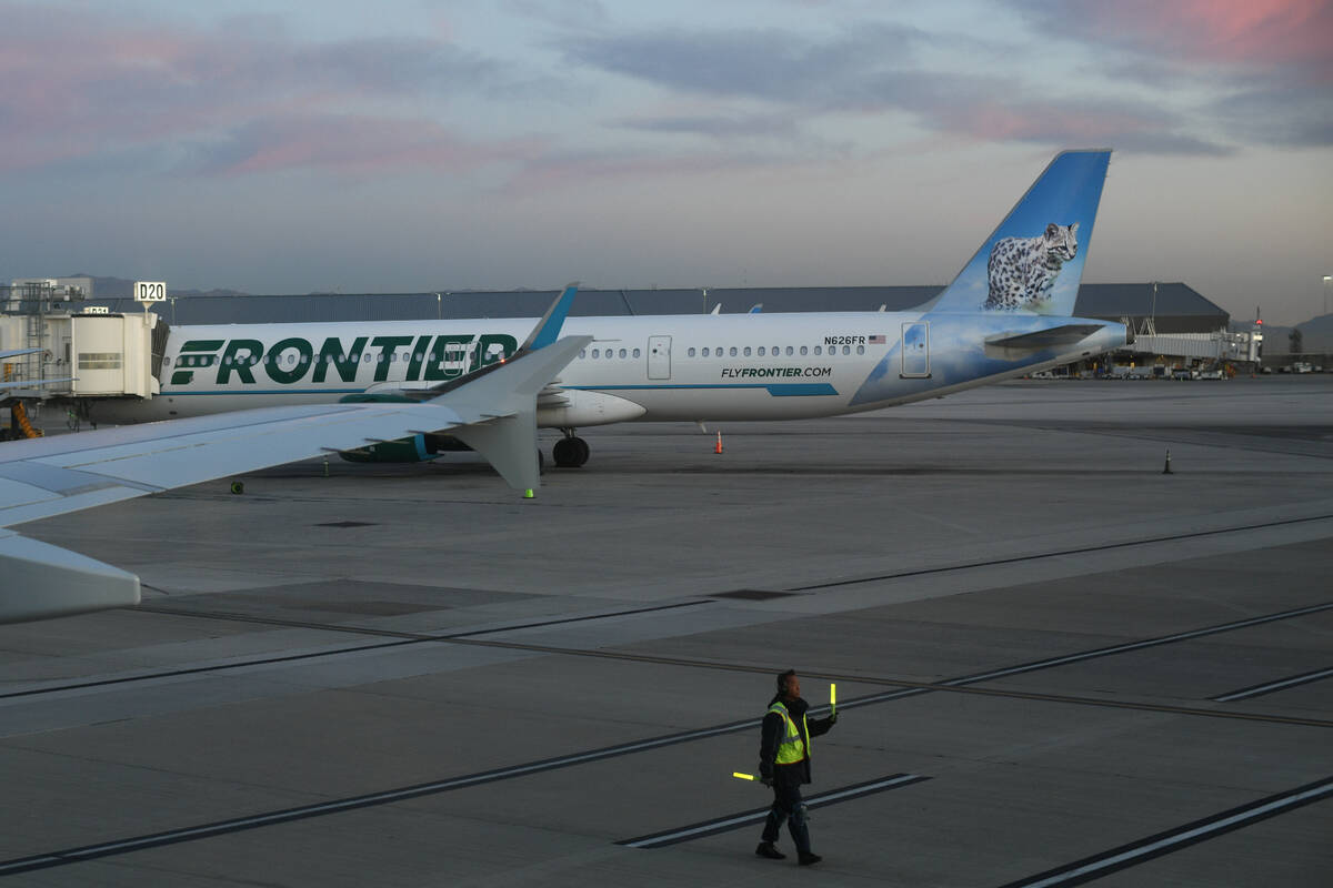 A ground crew member directs a plane back from a gate near a Frontier Airlines jet at Harry Rei ...
