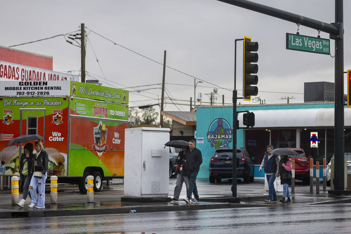People walk with umbrellas as rain trickles down along Las Vegas Boulevard near downtown Las Ve ...