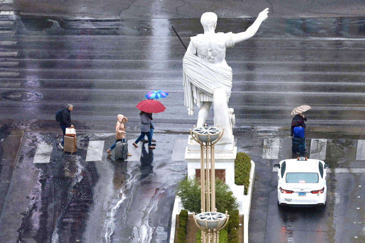 Pedestrians walk past a statue in front of Caesars Palace on the Strip during rainy weather in ...