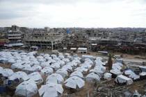 A sprawling tent camp for displaced Palestinians sits adjacent to destroyed homes and buildings ...
