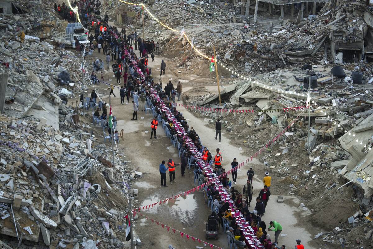 Palestinians sit at a large table surrounded by the rubble of destroyed homes and buildings as ...