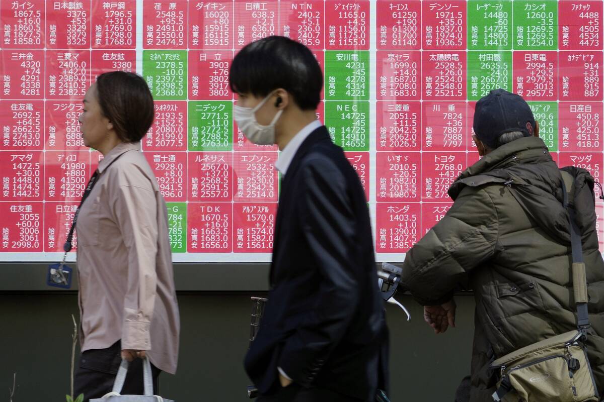 People walk in front of an electronic stock board showing Japan's Nikkei index at a securities ...