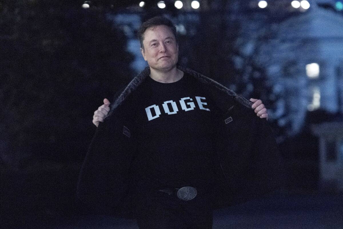 Elon Musk flashes his t-shirt that reads "DOGE" to the media as he walks on South Law ...