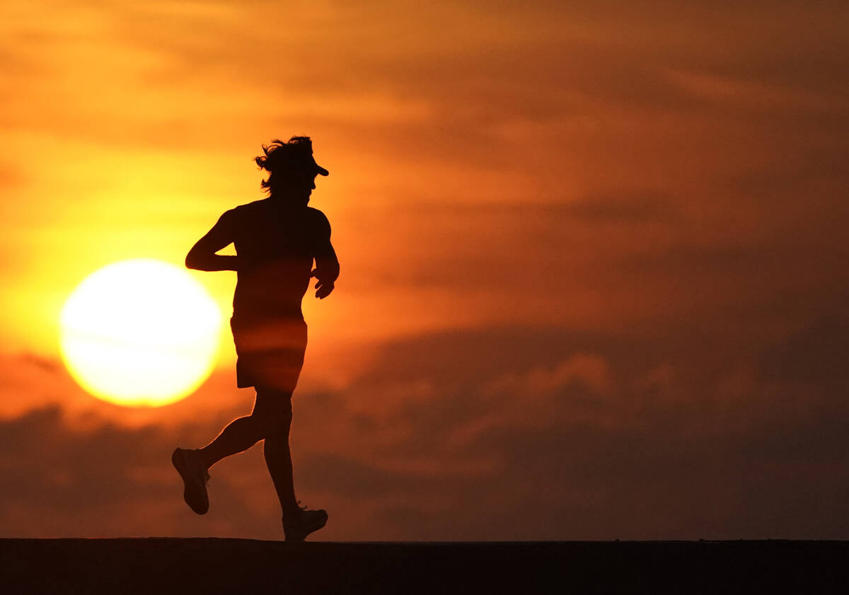 FILE - A jogger is silhouetted while running on a jetty at sunrise over the Atlantic Ocean in B ...