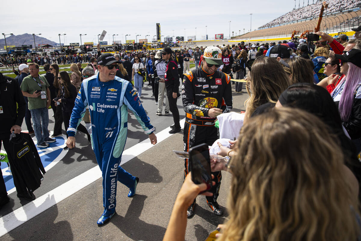 Driver Michael McDowell, left, walks by as driver Chase Briscoe (19) signs items for fans befor ...