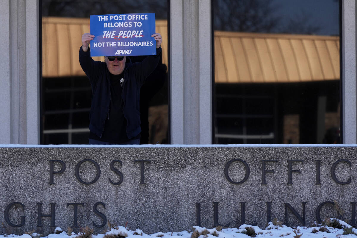A man holds a sign during a demonstration outside of the United States Postal Service in Arling ...