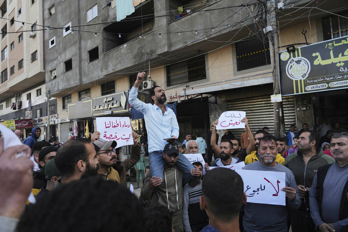Palestinians hold signs against the war as a man chants slogans in support of the people in Bai ...