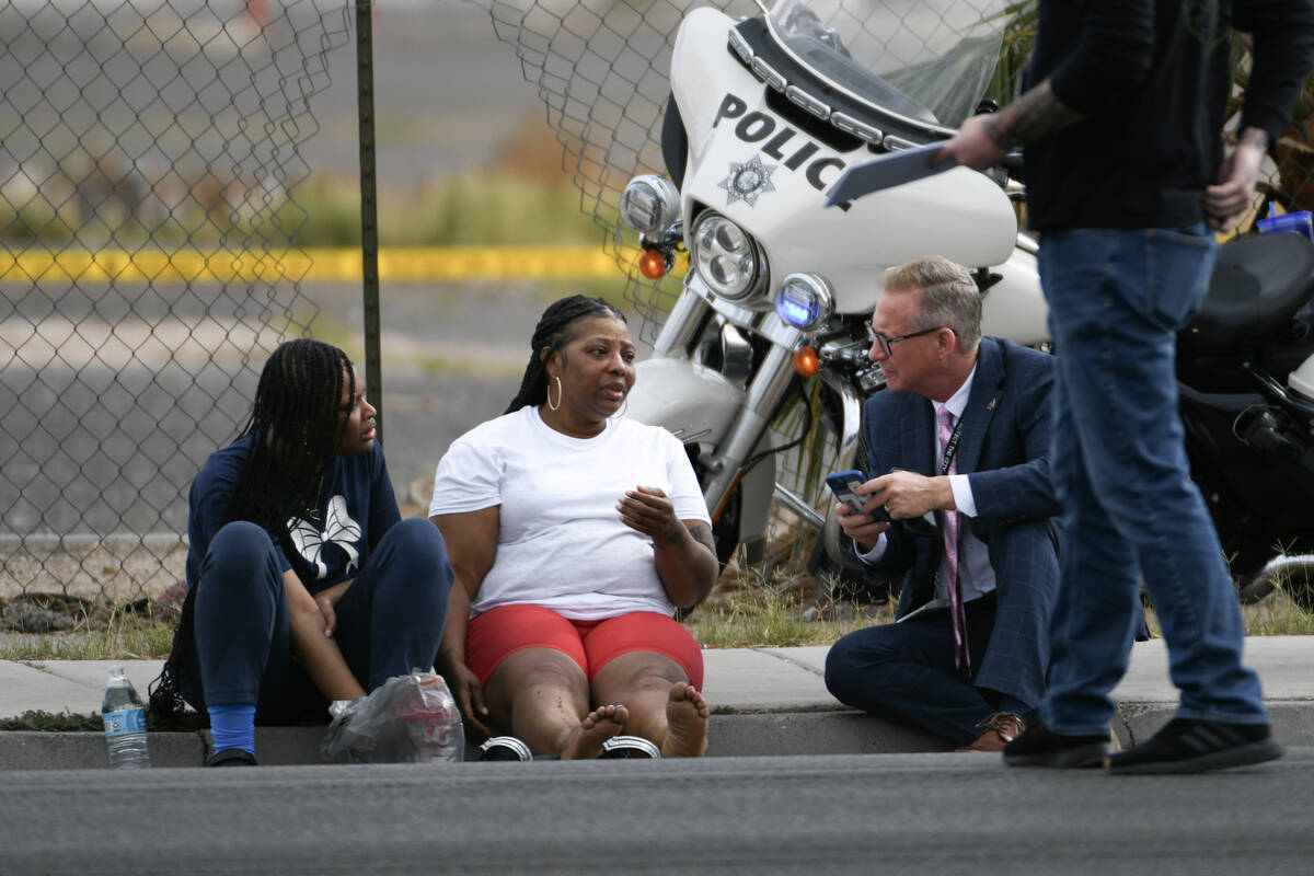 Two women sit on a curb and talk to a Metro detective while waiting for medical transport at th ...