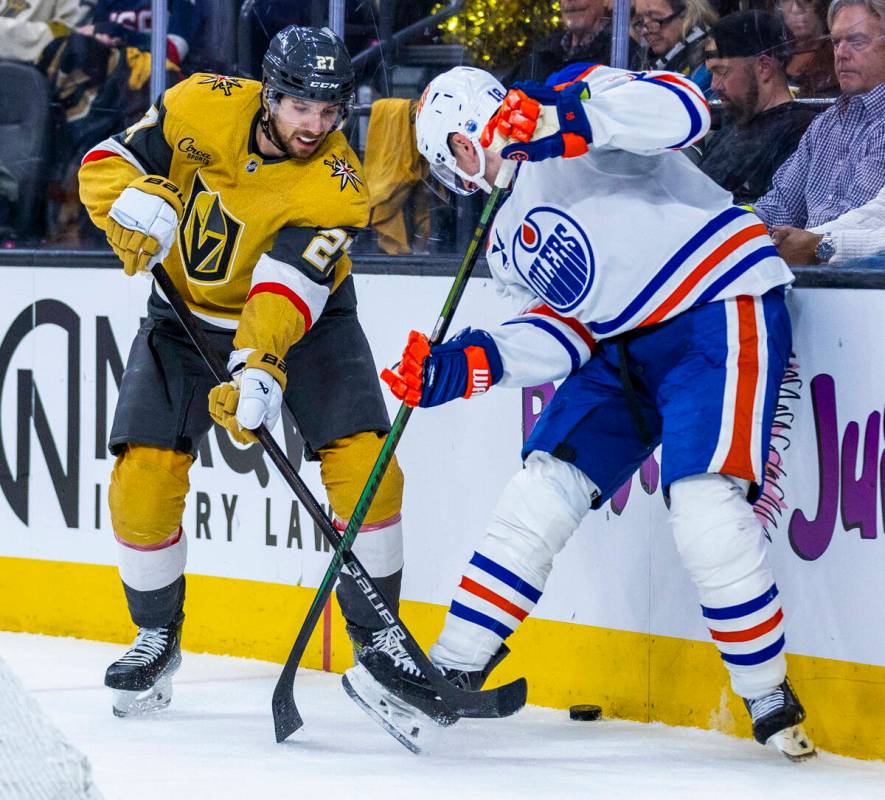 Golden Knights defenseman Shea Theodore (27) and Edmonton Oilers left wing Zach Hyman (18) batt ...
