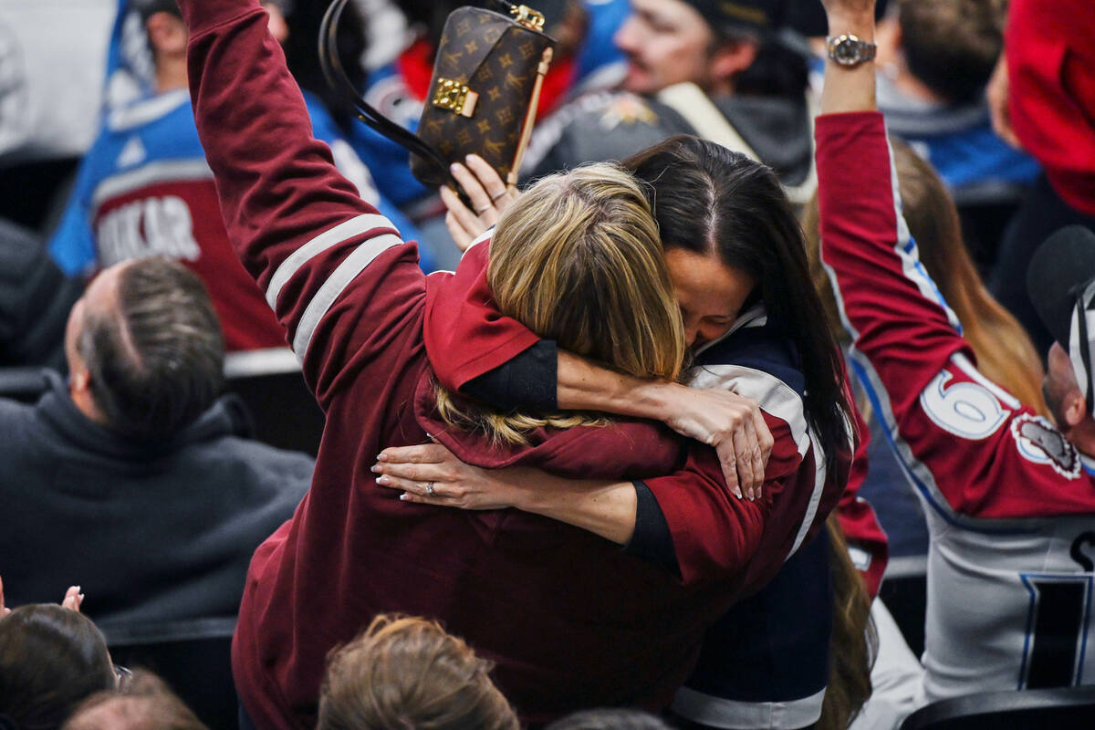 Fans of the Colorado Avalanche embrace after catching a puck that went into the stands during o ...