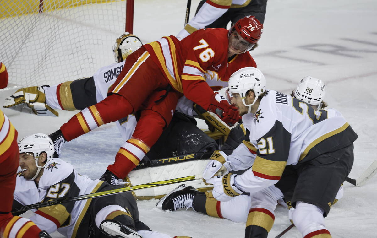 Vegas Golden Knights' Alexander Holtz (26) and Brett Howden (21) check Calgary Flames' Martin P ...