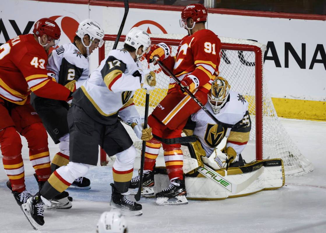 Vegas Golden Knights' Ben Hutton (17) checks Calgary Flames' Nazem Kadri (91) into goalie Ilya ...
