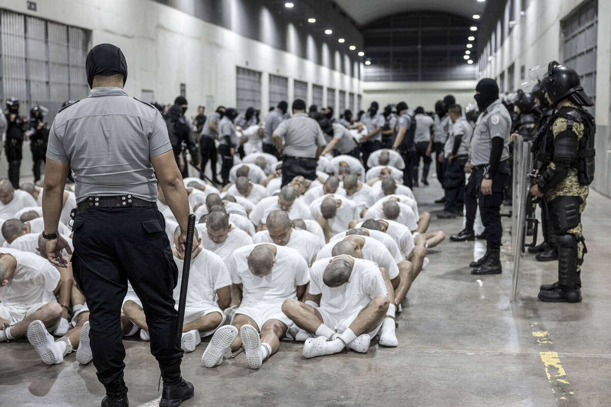 In this photo provided by El Salvador's presidential press office, a prison guard transfers dep ...