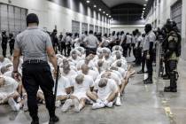 In this photo provided by El Salvador's presidential press office, a prison guard transfers dep ...