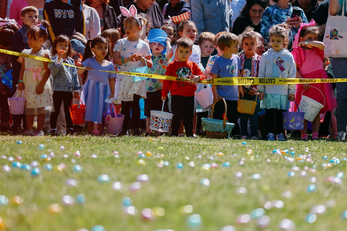 Children aged three to four wait for their turn to run out onto the lawn to collect their eggs ...