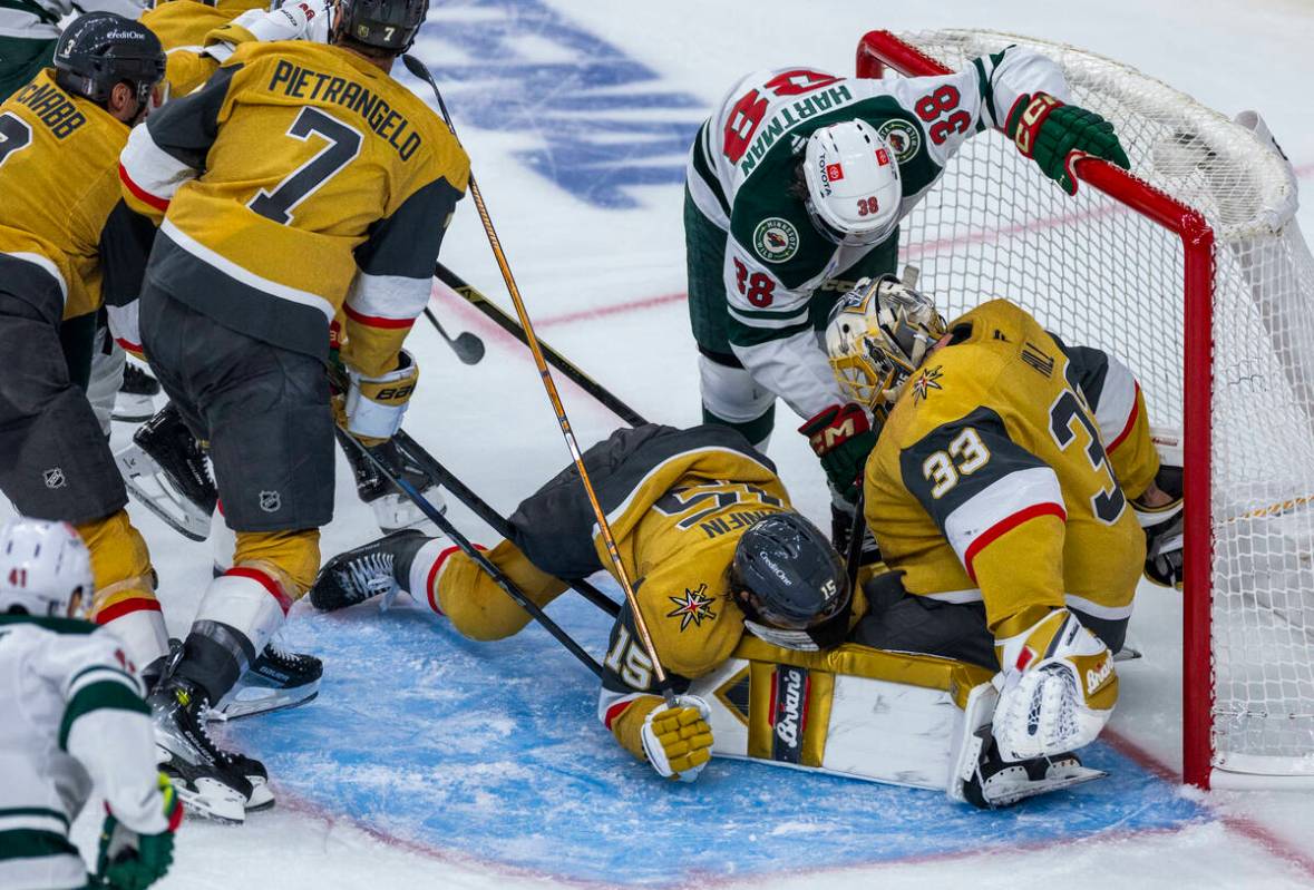 Golden Knights defenseman Noah Hanifin (15) is pushed down onto goaltender Adin Hill (33) as Mi ...