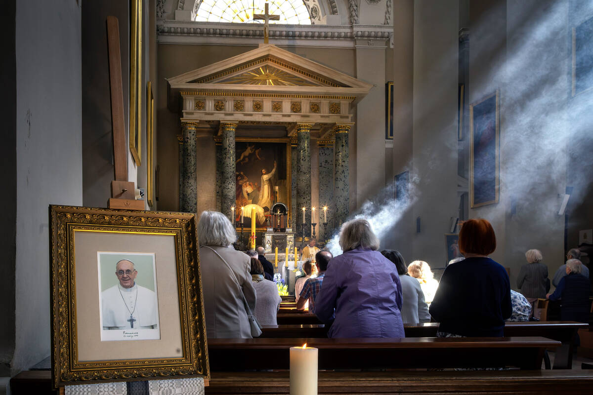 People pray next to a photograph of Pope Francis placed at Cathedral Basilica of Vilnius, Lithu ...