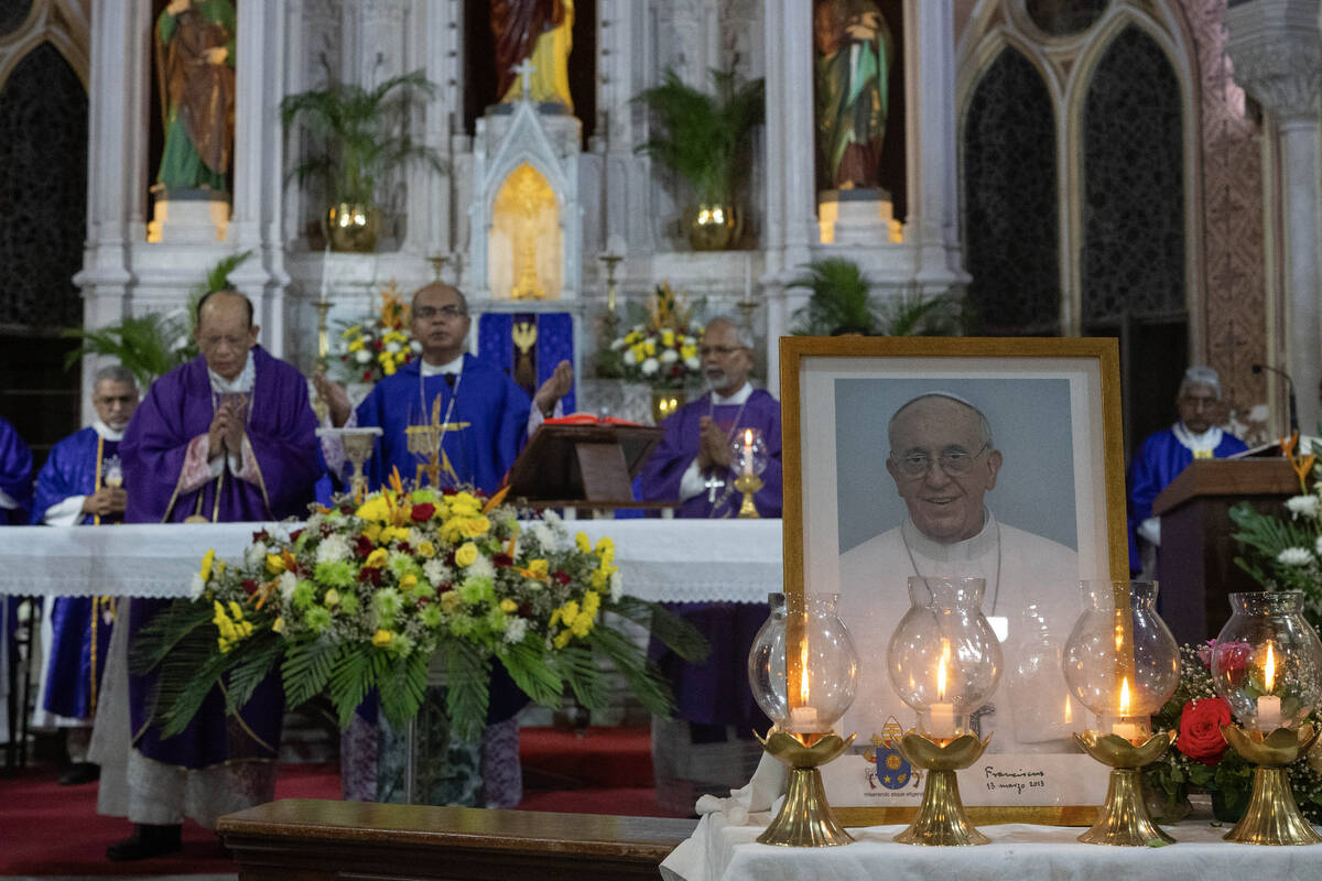 Catholic priests offer prayers in front of a photograph of Pope Francis during a mass at a chur ...