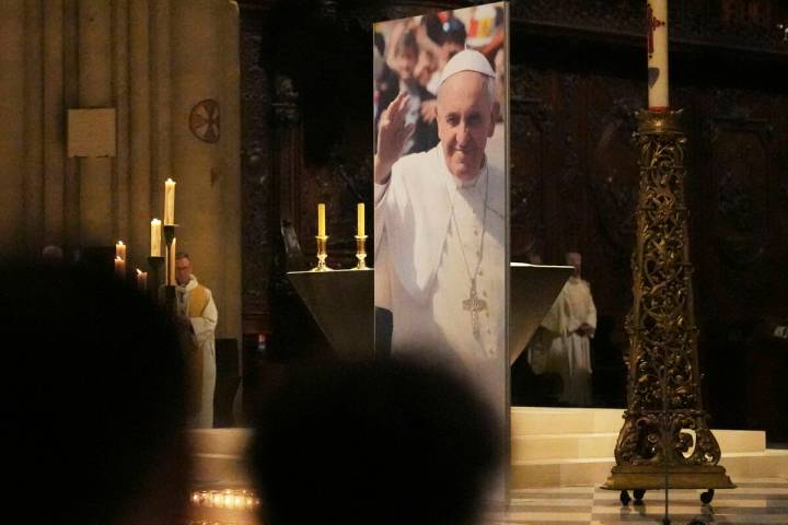 People attend a ceremony inside Notre Dame cathedral where a poster shows Pope Francis followin ...