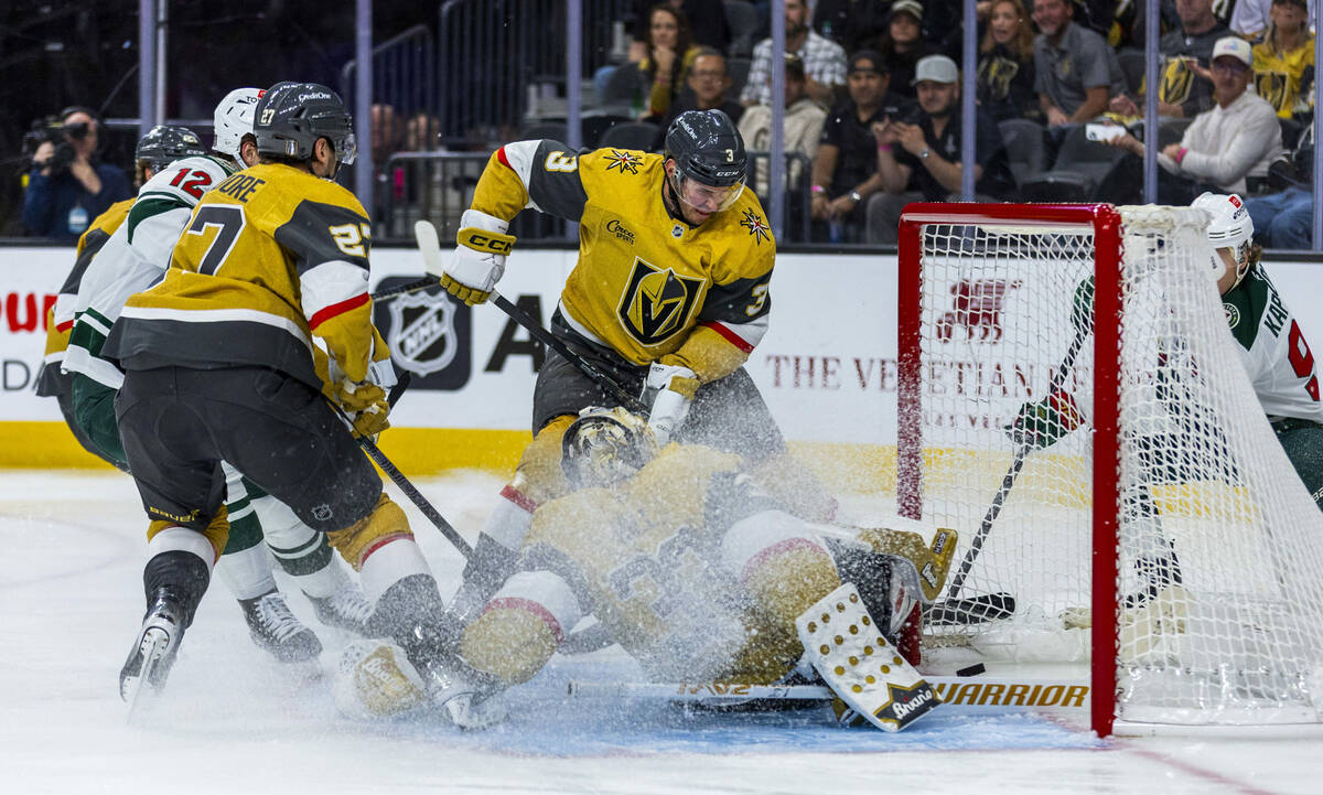 The puck sneaks by Golden Knights goaltender Adin Hill (33) as he collides with defenseman Bray ...