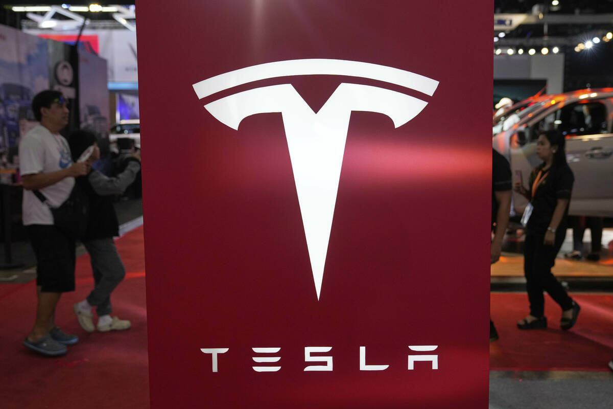 People pass by a Tesla sign at the Manila International Auto Show in Pasay city, Philippines Fr ...