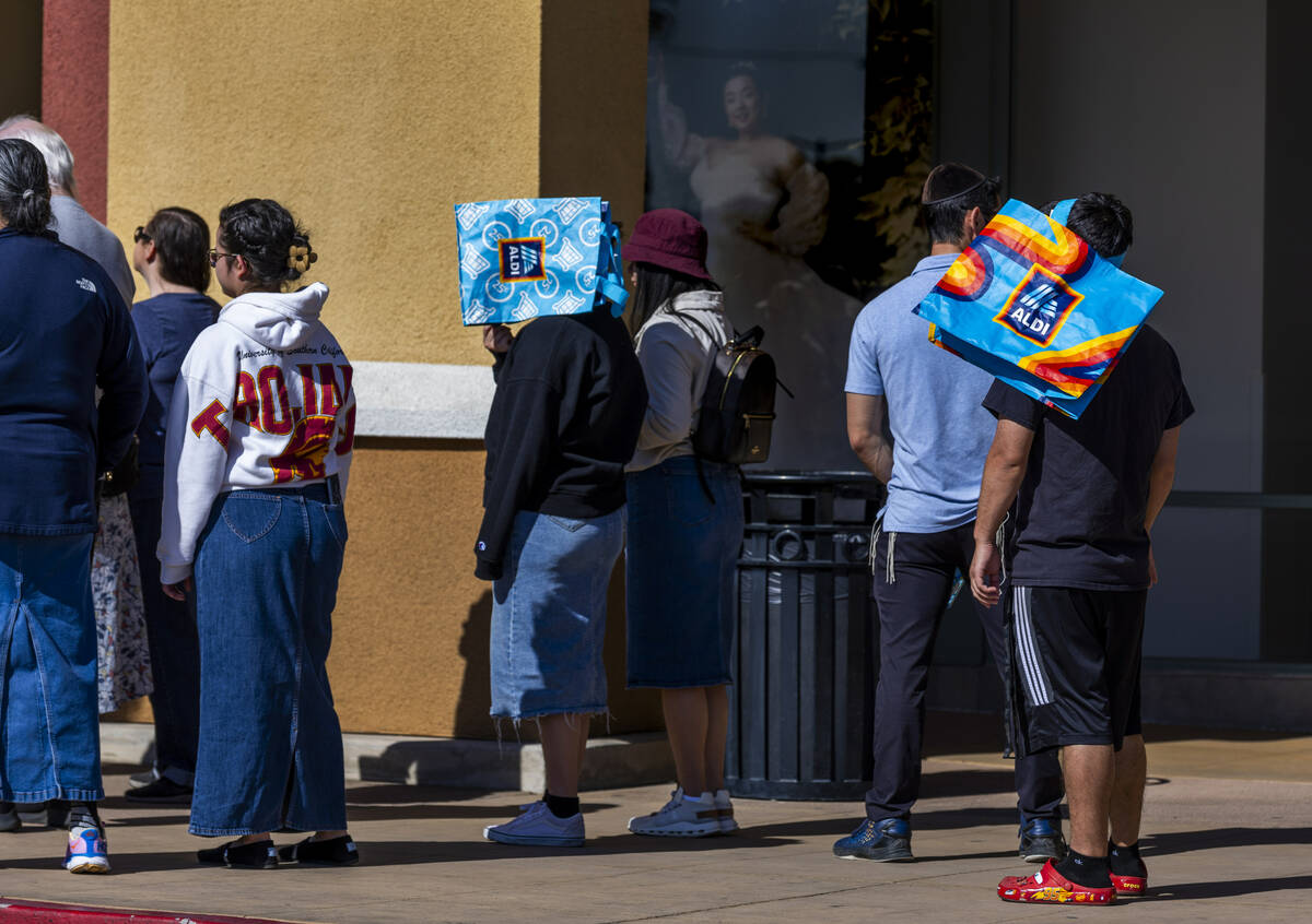 Customers keep the sun off their faces while waiting in line to shop in the new store as Aldi i ...