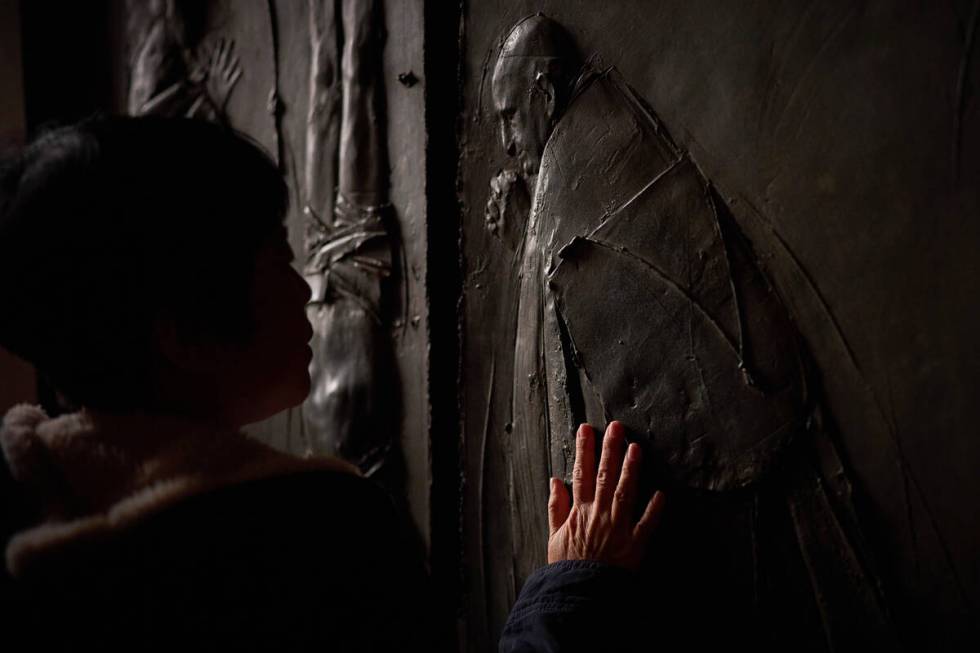 A woman places her hand on the entrance door of St. Peter's Basilica where Pope Francis lying i ...