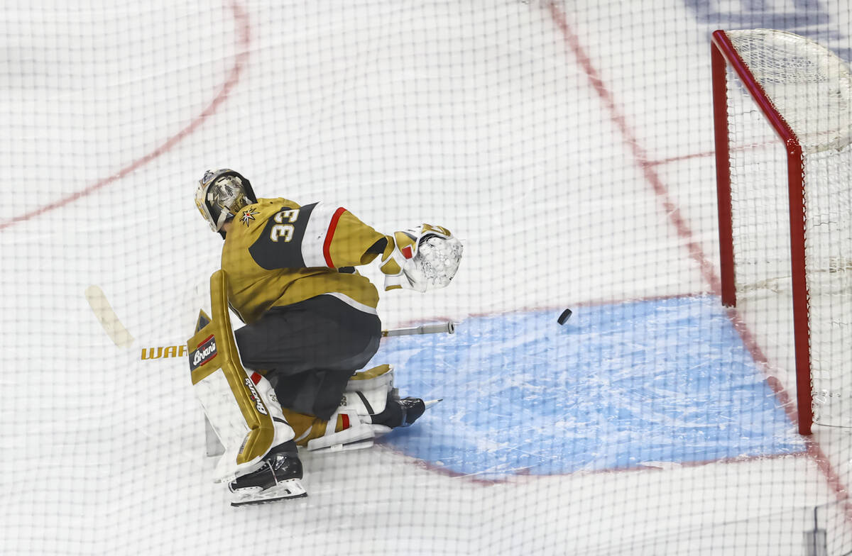 A deflected puck slides past the goal post as Golden Knights goaltender Adin Hill (33) looks on ...