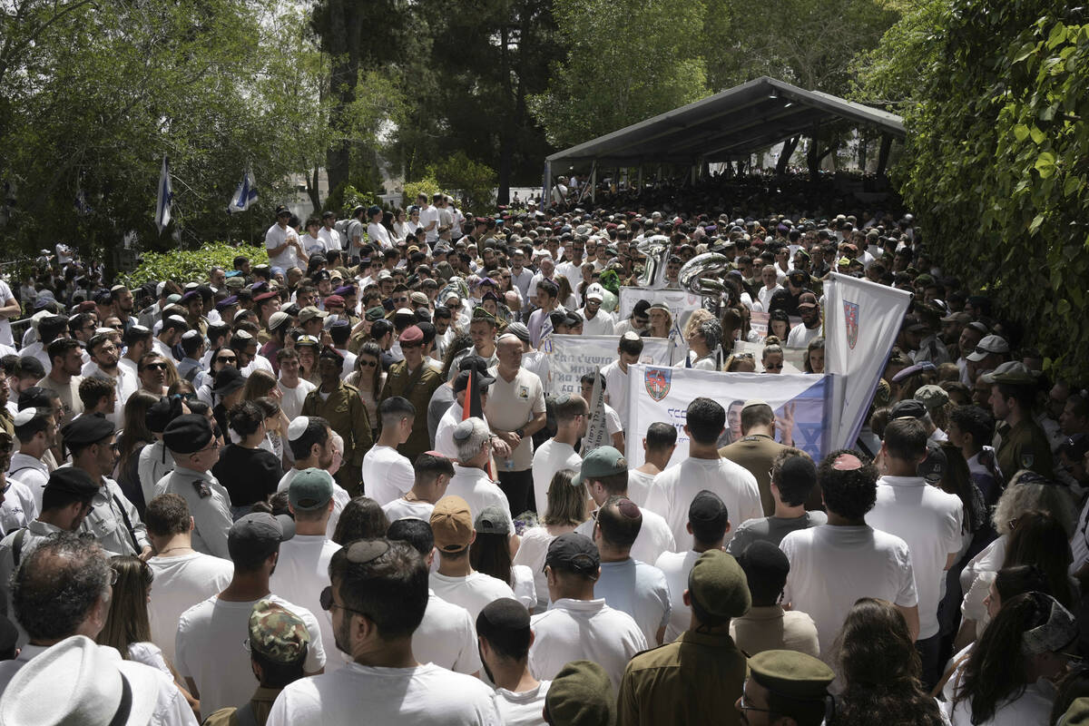 People and Israeli soldiers stand during two minutes of silence as air raid sirens sound markin ...