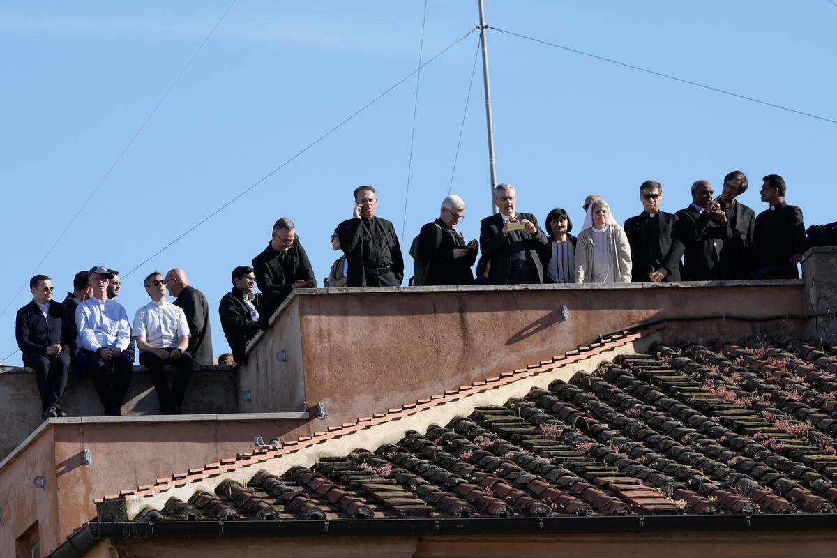 Clergy stand on a rooftop terrace as they wait to see the smoke billow from the chimney of the ...