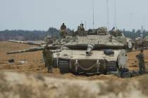 Israeli soldiers work on tanks and APCs at a staging area near the border with the Gaza Strip, ...