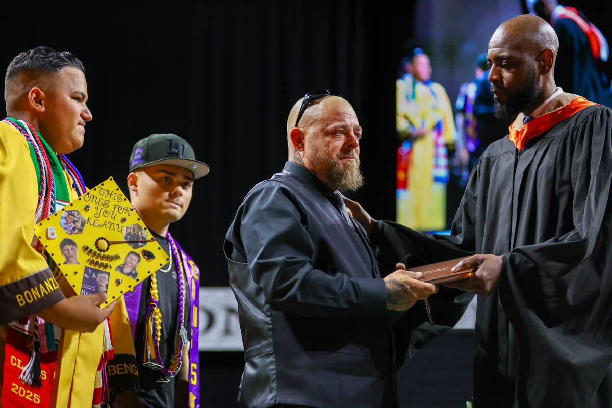 Thomas Enright, center, accepts his son Keanu’s diploma from Bonanza High School assista ...