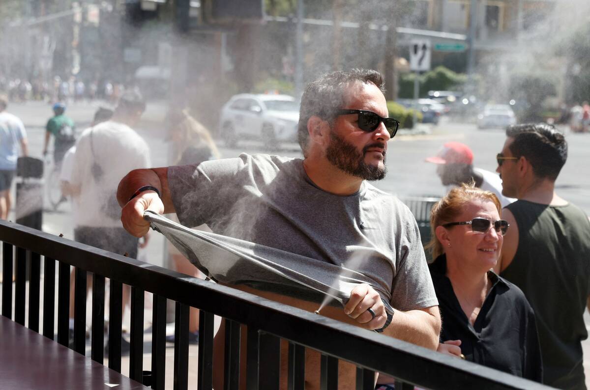As the temperature climbs towards triple digits, a pedestrian cools off with water misters alon ...