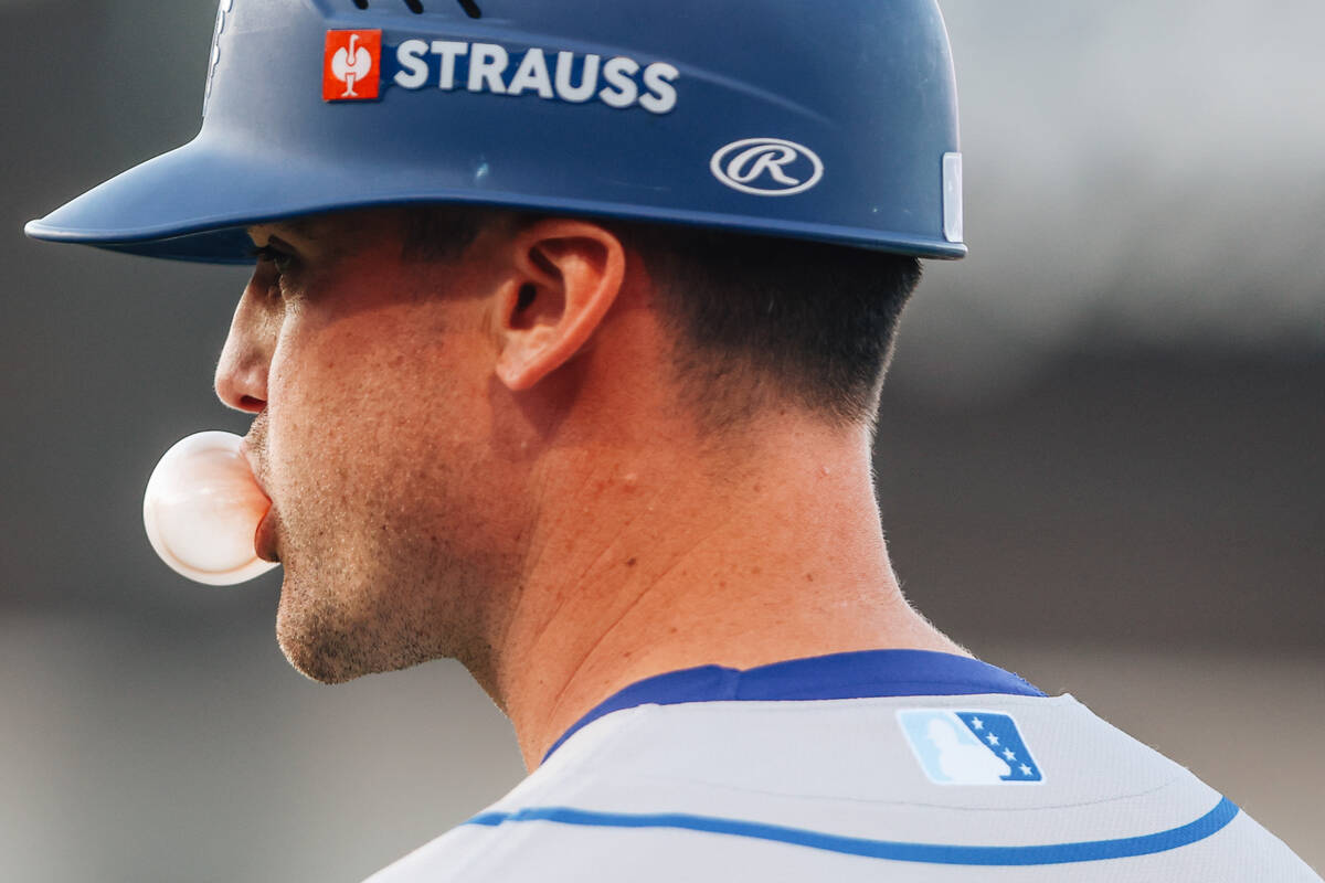 Oklahoma City Comets first base coach Tyler Hollow blows a bubble with his bubble gum during a ...