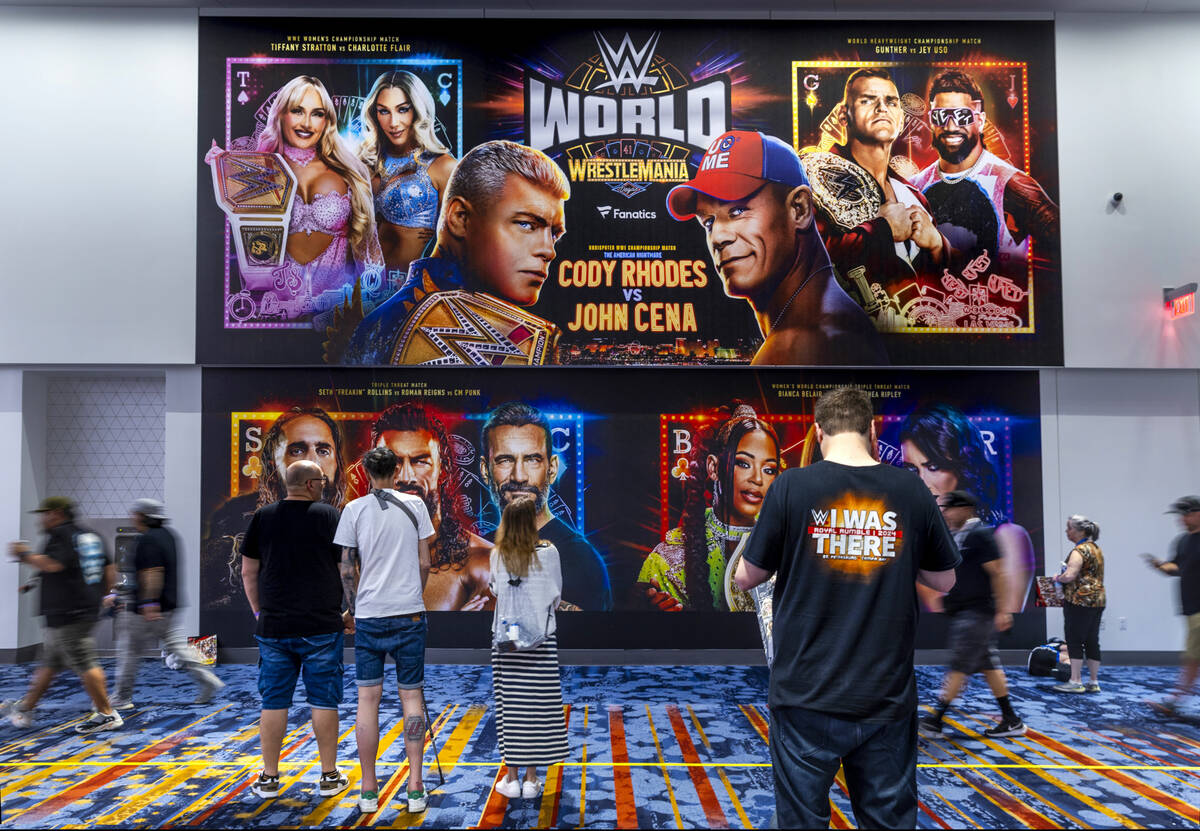 A massive poster hangs on the wall as fans stream by at WWE World, the Ultimate Fan Experience ...