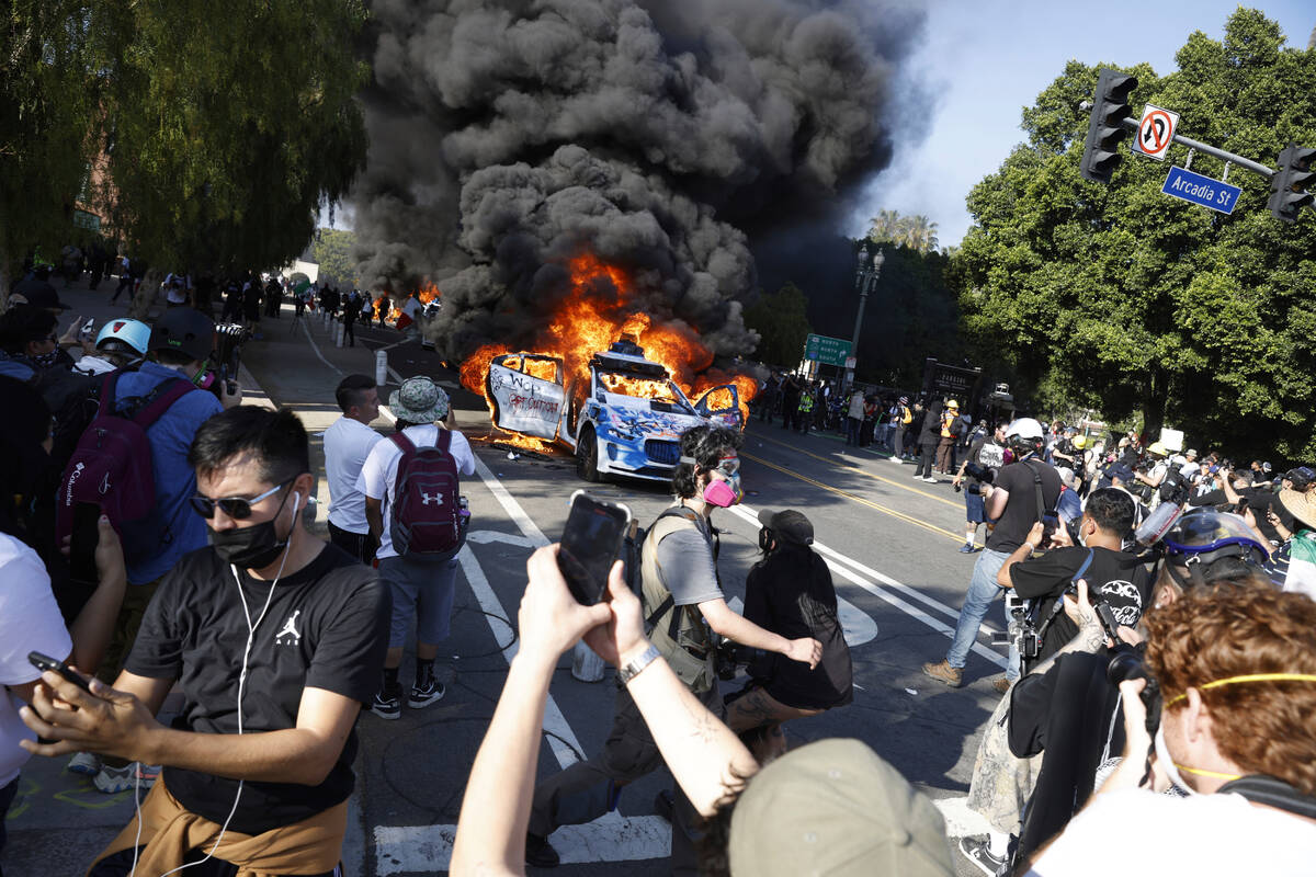 People watch while several Waymo cars burn in downtown Los Angeles after being vandalized by pr ...