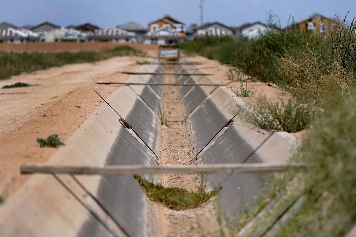 A dry irrigation canal runs between two unplanted fields as new home construction abuts dormant ...